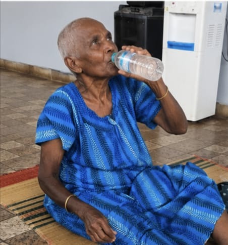 Gangammal drinking clean water from a bottle at the shelter